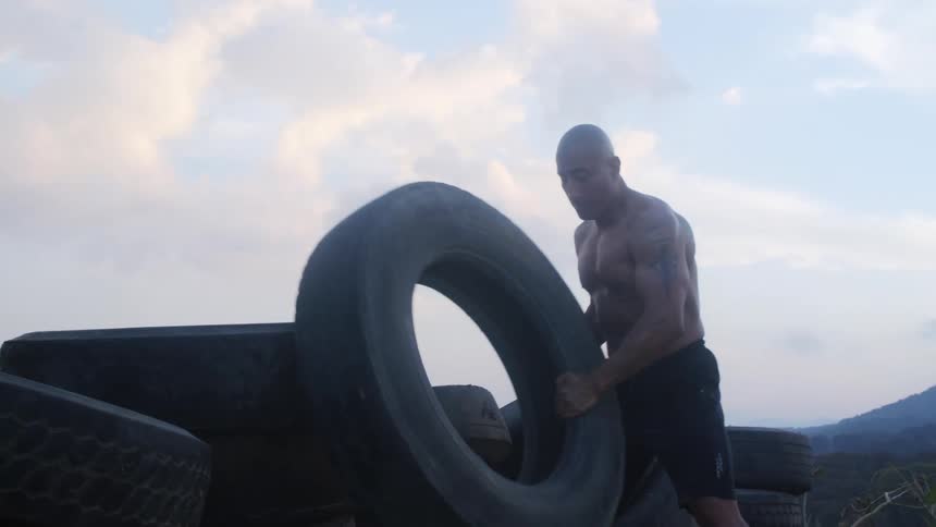 Man lifting a big black tire off of a stack of other black tires at daytime outdoors