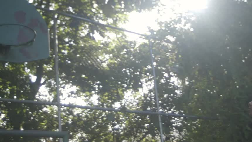 Girl shoots a basketball to a hoop missing a net on a basketball court in the park