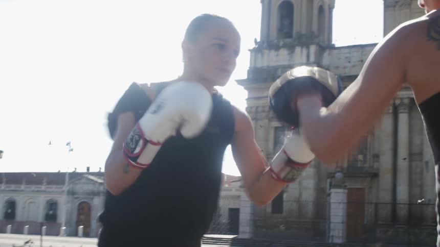 Two women are boxing outdoors in a city