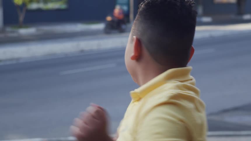 A boy pretends to box standing on the corner on a street while a woman jogs past