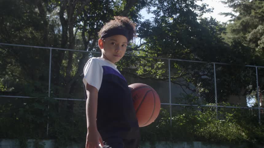 Young girl holding a basketball on a court looking at the camera
