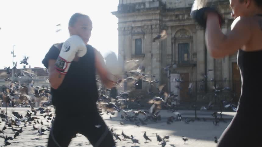 A woman boxes with a trainer in a town square outdoors at daytime