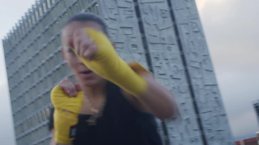 Woman wearing yellow hand wraps throwing punches in the air outdoors at day time