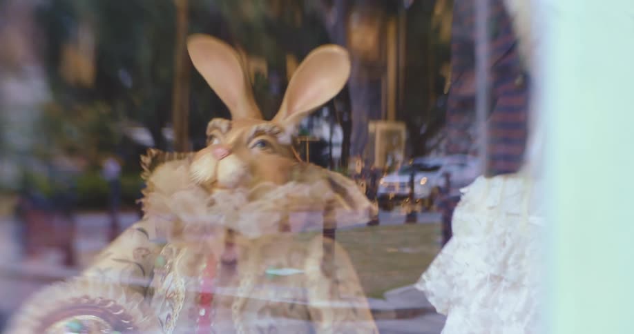 A car drives past a store with clothing and a sculpture in the window