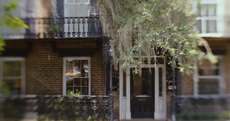 Exterior of a historical two story home at daytime with spanish moss overgrowths at the doorway
