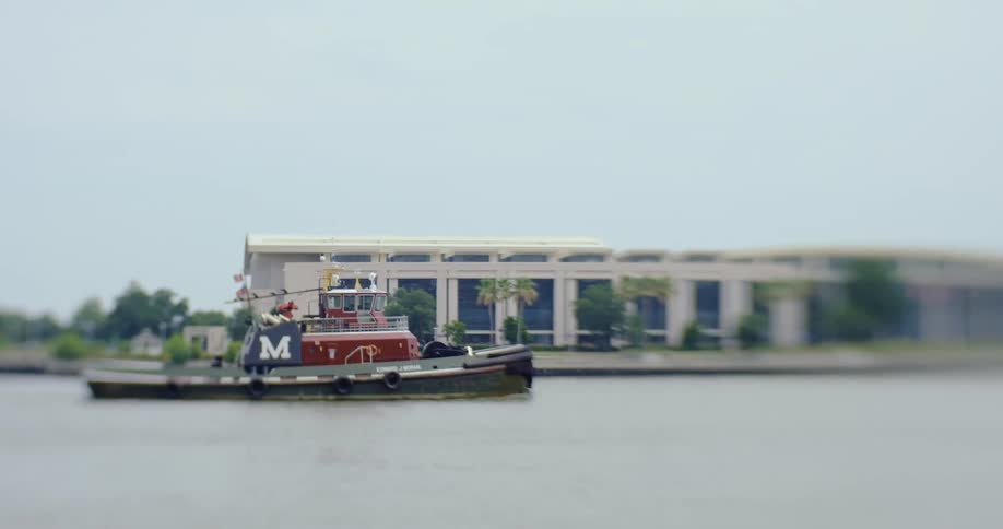 A tugboat slowly passes by a building that is built right on the edge of the water