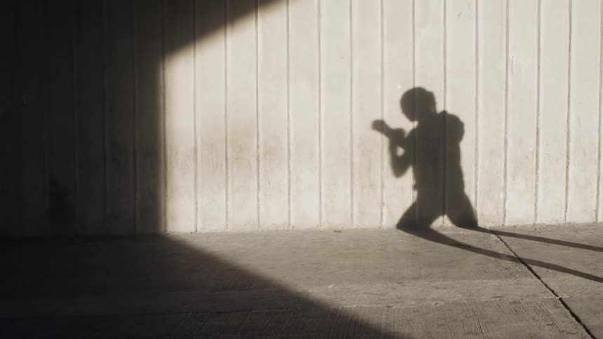 Shadow on a wall of woman practicing boxing punches outdoors