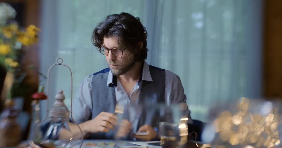 A man is seated at a table and is placing cards on it
