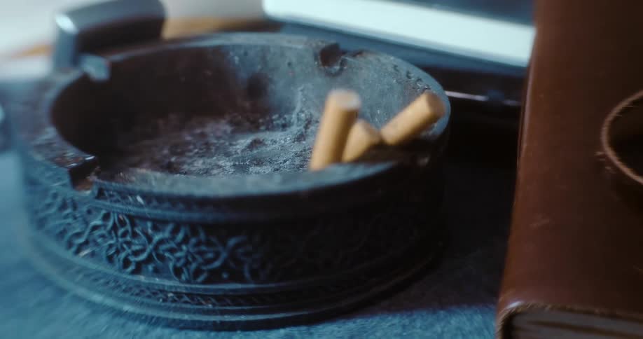 Cigarette stubs rest in a black stone ashtray on a table during the day