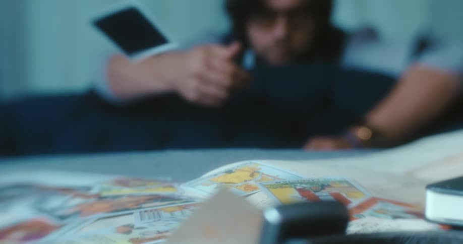Man tosses a tarot card over into a stack of cards on a table