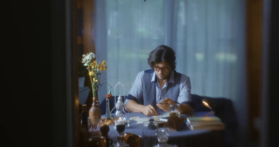A man sits indoors at a table looking and placing cards on the table