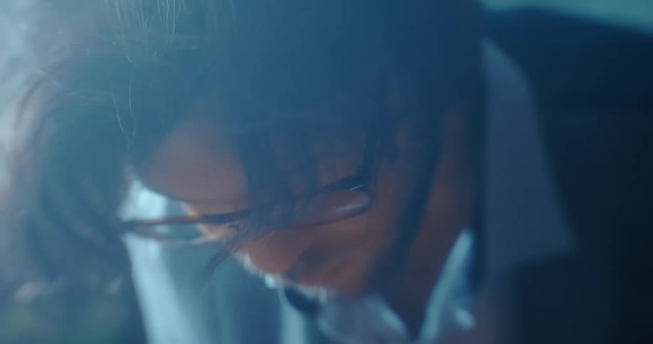 A man with a beard and glasses looks down as he is deeply focused on his task