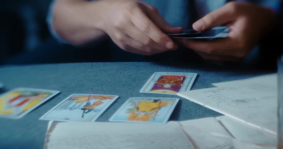 A man sits at a table flipping cards face up with papers and a glass in front of the row of cards