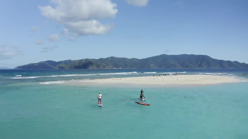 Three men on paddleboards at daytime out in the middle of the ocean next to a very small islet