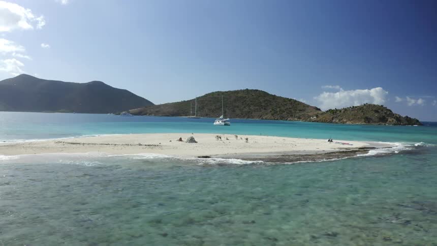 A sand bar visible in the middle of the ocean surrounded by hills and a boat