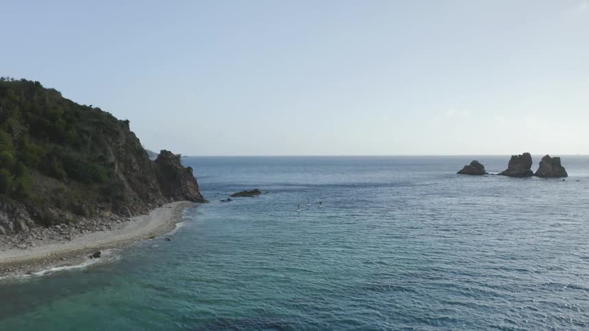 Three people on paddle boards paddling next to a shore at daytime out in the ocean