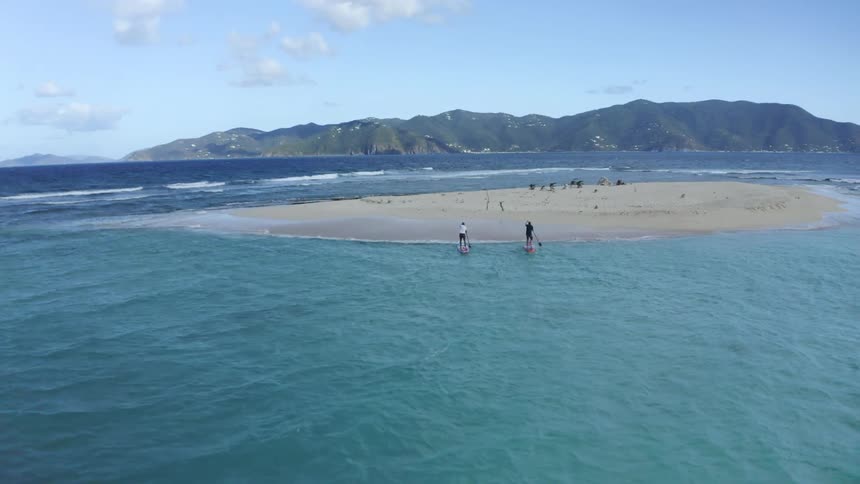 Two people paddle boarding near the coast with a mountain range the sky and clouds in the background