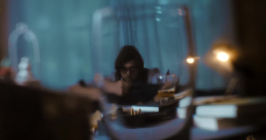 A man sits at a table indoors at night picks up a card looks at it then throws it across the room