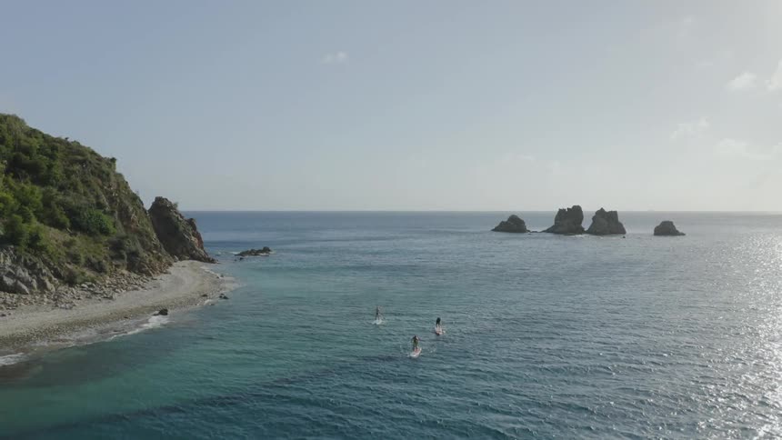 The sun shines on an ocean and three people are paddle boarding in it