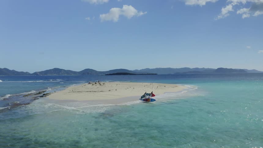 Three people on a small island carry surfboards and place them over in water in the ocean at daytime