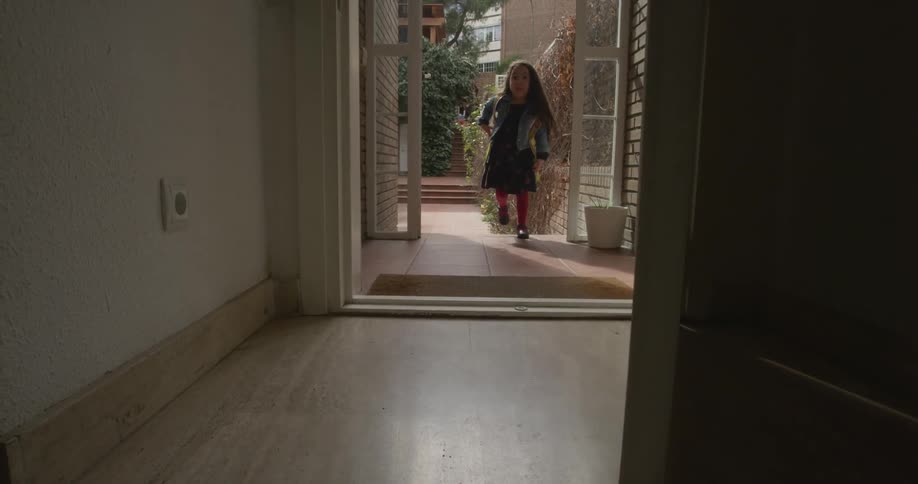 Front door of a home opens and a little girl wearing a backpack walks in and puts it down