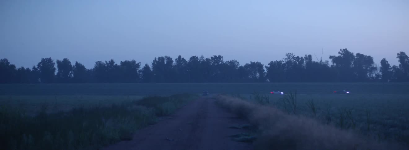 Car parked at the end of a dirt road in the evening in front of a highway where cars are driving by