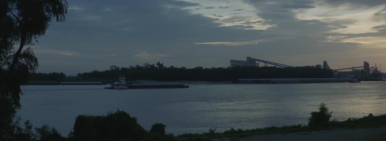 An empty barge driving down a river in front of a city view in the evening