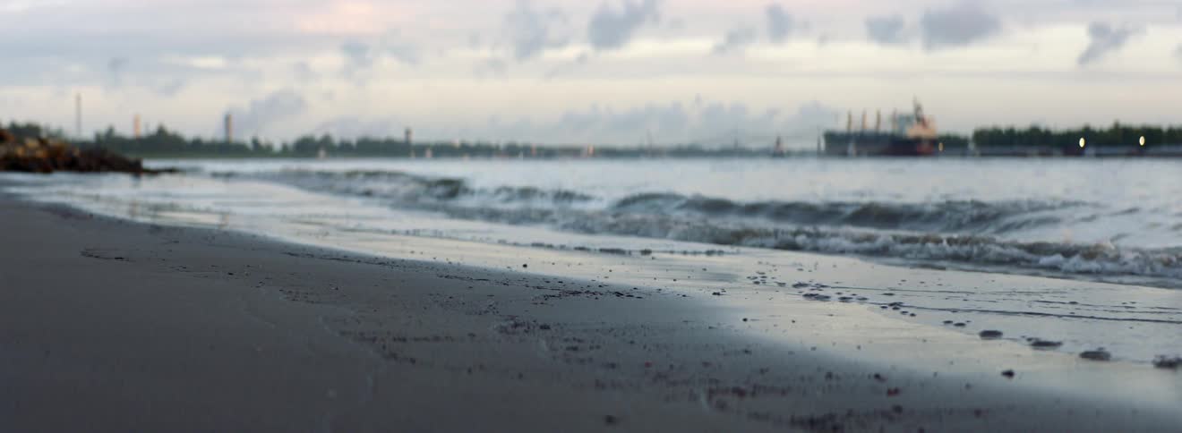 Small waves repeatedly wash up upon a sandy beach under a cloudy sky