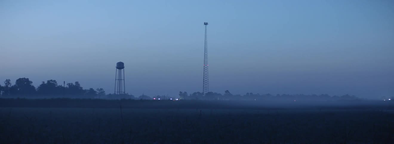 Landscape with trees a water tower steel tower and hills at night