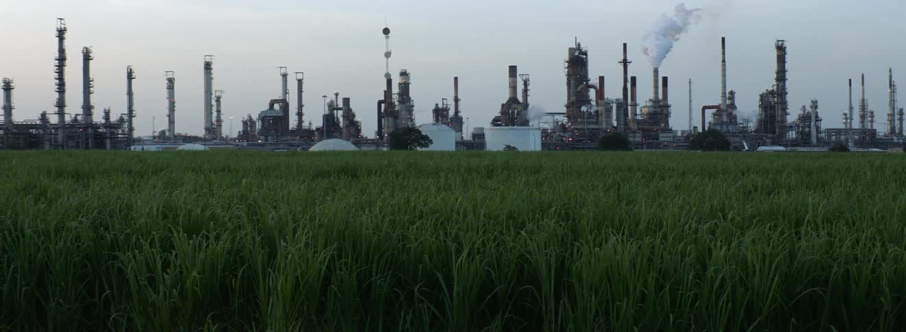 Industrial factory in the distance behind a field of short grass at daytime