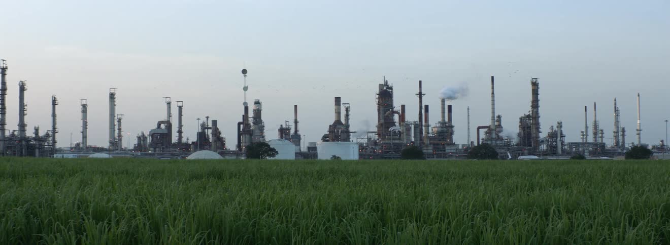 Next to a wide open grass field is a massive refinery facility