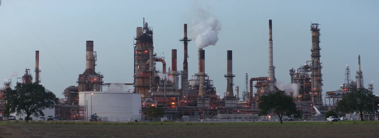 The outside of a refinery with smoke billowing out of a stack