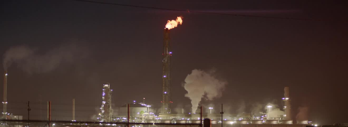 A large flame is let off of the top of a tall tower at refinery facility
