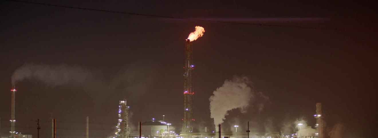Large factory with fire and smoke blowing from its roof exhaust at nighttime