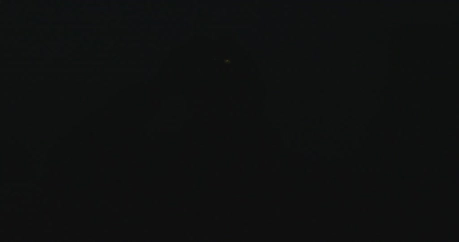 A person with a jacket and a flashlight on their head turning it off in the darkness