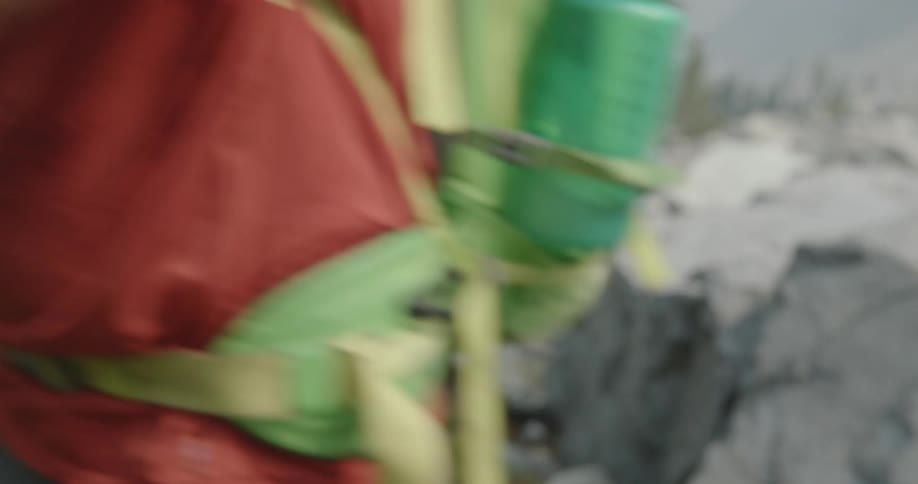 A man is backpacking and grabs the handles of hiking gear outdoors in front of a path and rocks