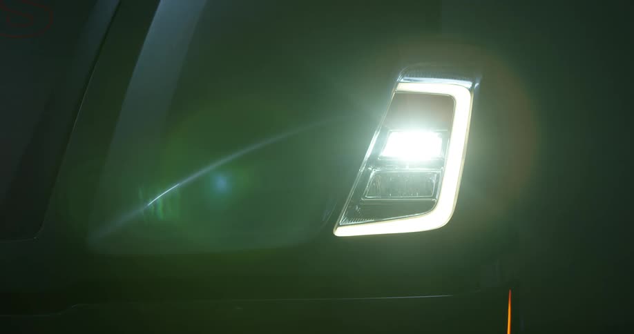 A vehicle with a sleek design sits idly in the darkness when a headlight turns on