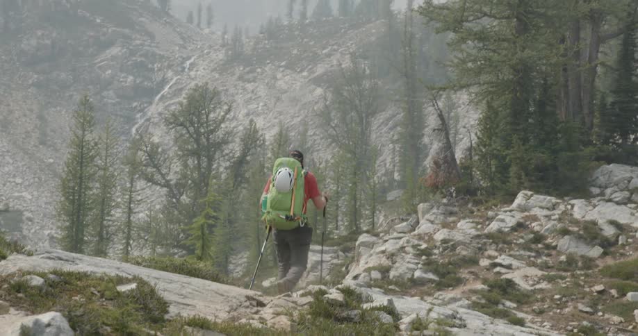 Man wearing hiking equipment hiking up a hill at daytime with two walking sticks