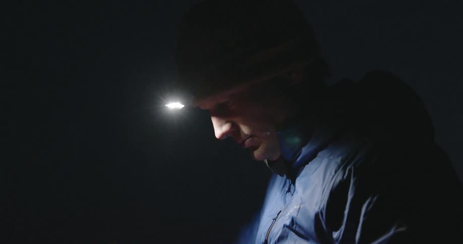 Man wearing a headlamp at night struggling with a bag in his hand