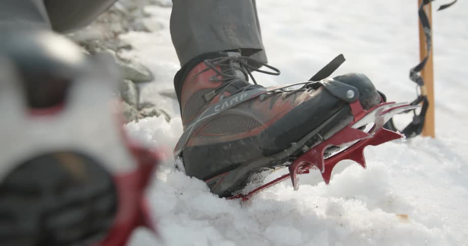 A person ties shoes on with spikes to hike in the snow