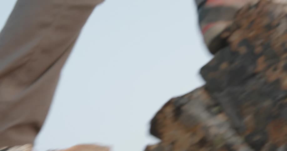 A person with boots walking on a rocky cliff with the sky and clouds in the background