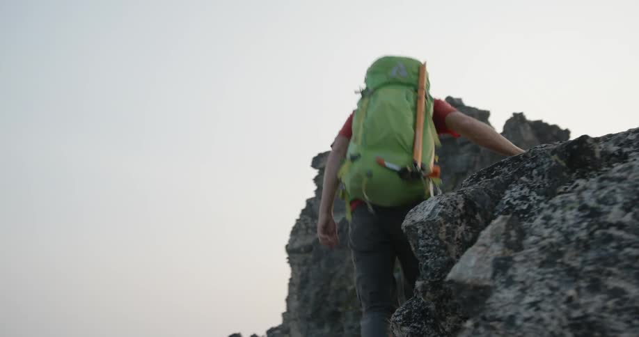 A man carrying a large backpack swiftly hikes up a rocky mountain landscape