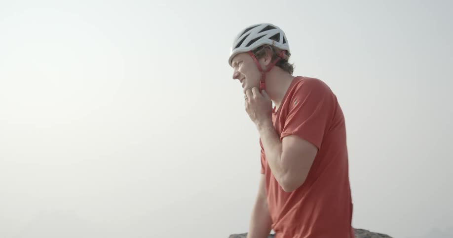 A man is hiking and stops to remove his backpack and helmet for a rest near a rock