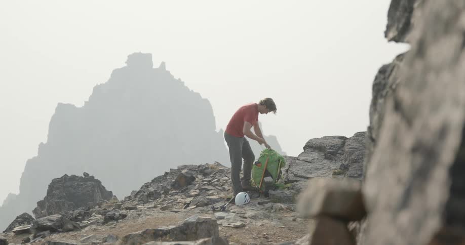 A man stands on the side of a mountain and takes out a shirt from a bag