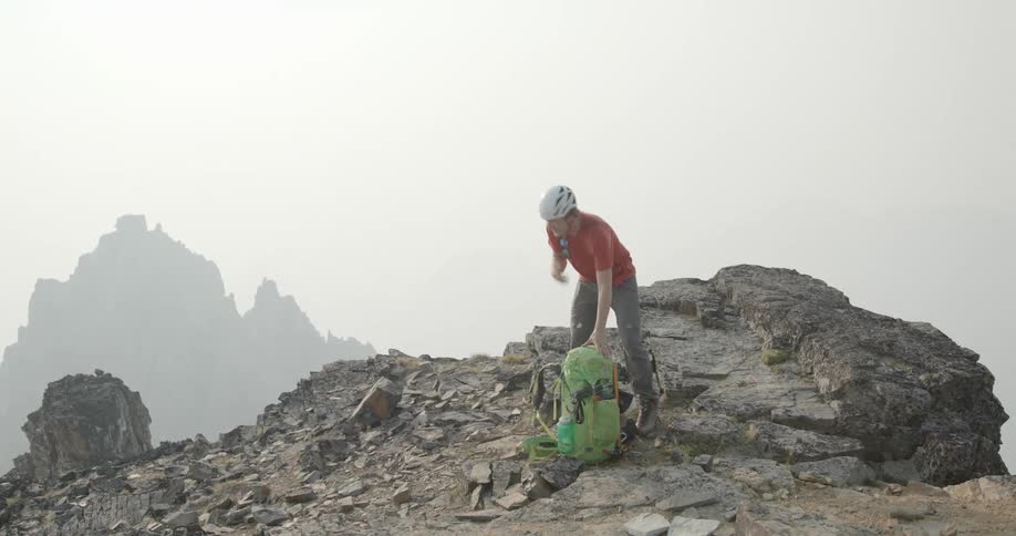 Man drops green backpack on the mist covered mountain top