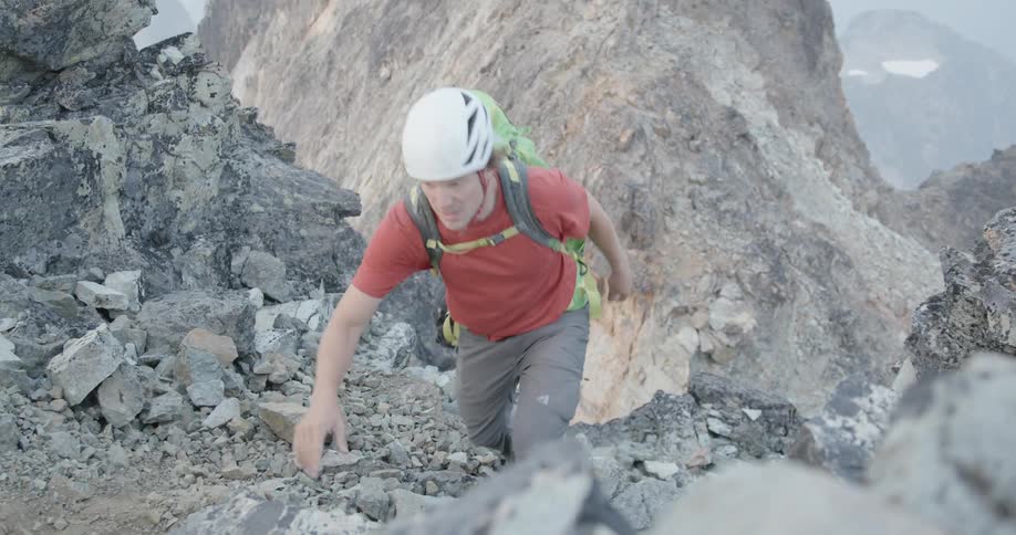 A man is climbing up a mountain during the day