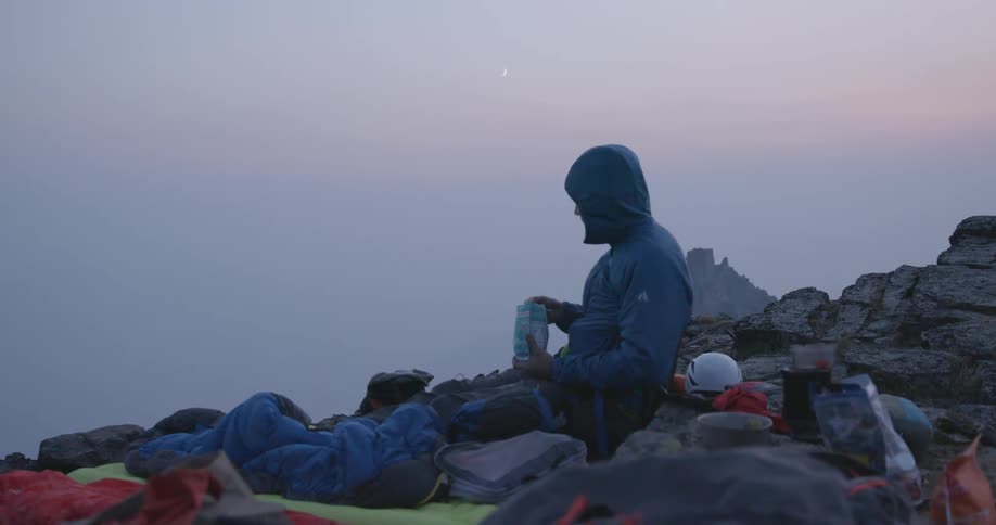 A man sitting and eating from a bag on top of a mountaintop