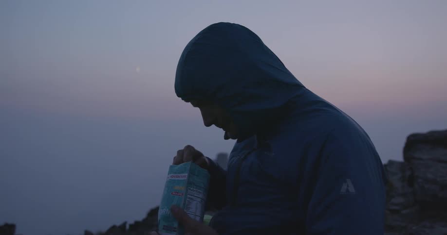 A shot of a man eating food from a bag outside at dusk