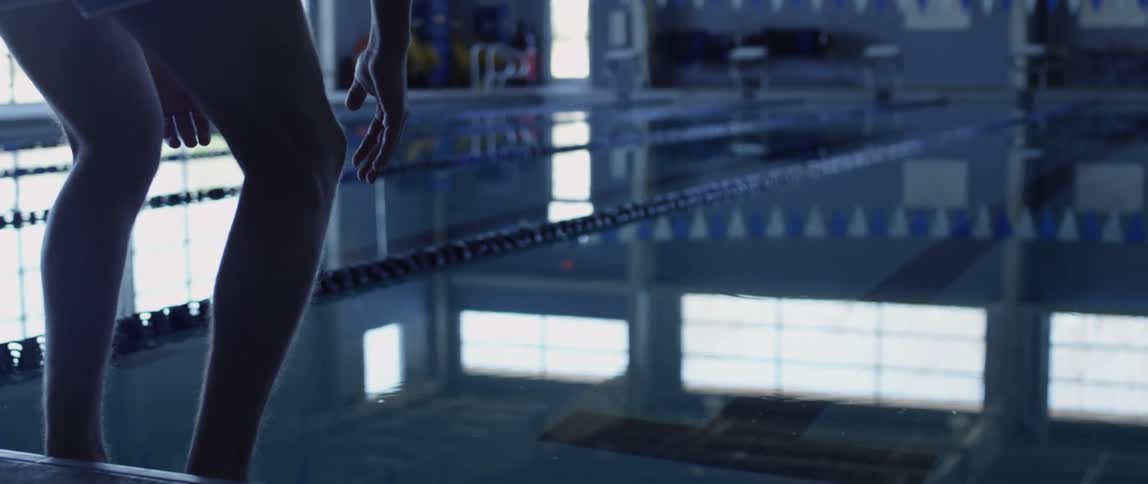 A person with shorts crouching in front of a pool