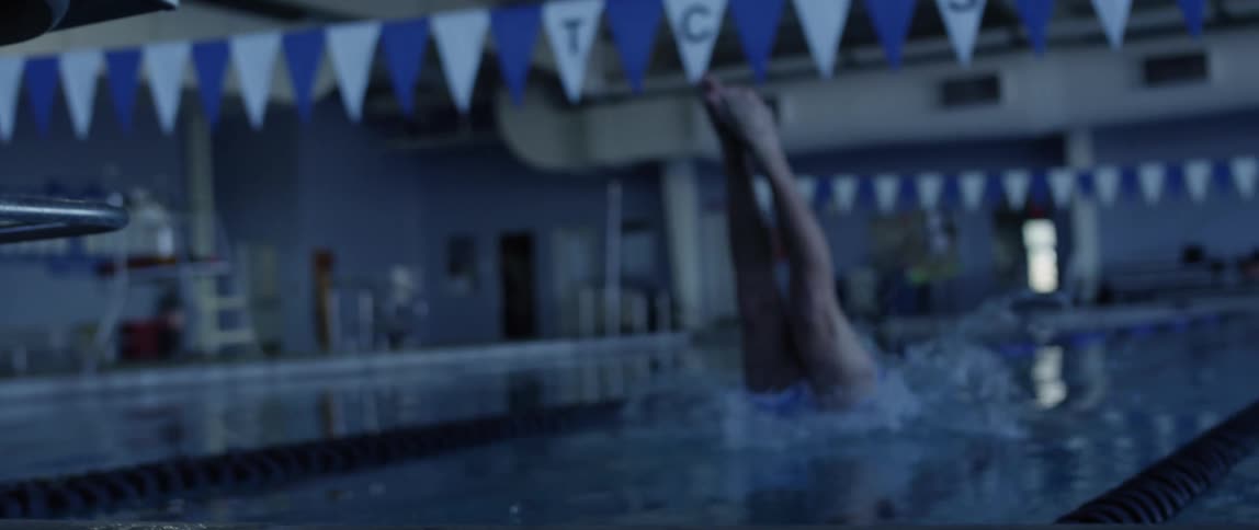 A man with shorts diving into a pool from a platform and splashing water
